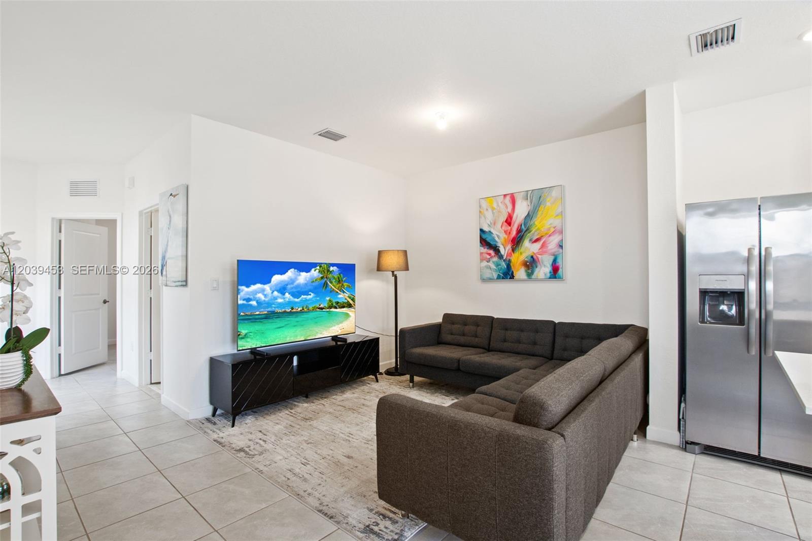 A living room features a dark sectional sofa, a television on a stand, and tile flooring — 23391 SW 128th Ave, Homestead FL 33032, HOMESTEAD, FL