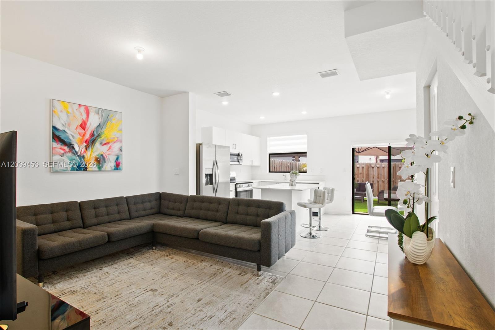 A living room with a grey sectional sofa flows into an open kitchen with white cabinets — 23391 SW 128th Ave, Homestead FL 33032, HOMESTEAD, FL