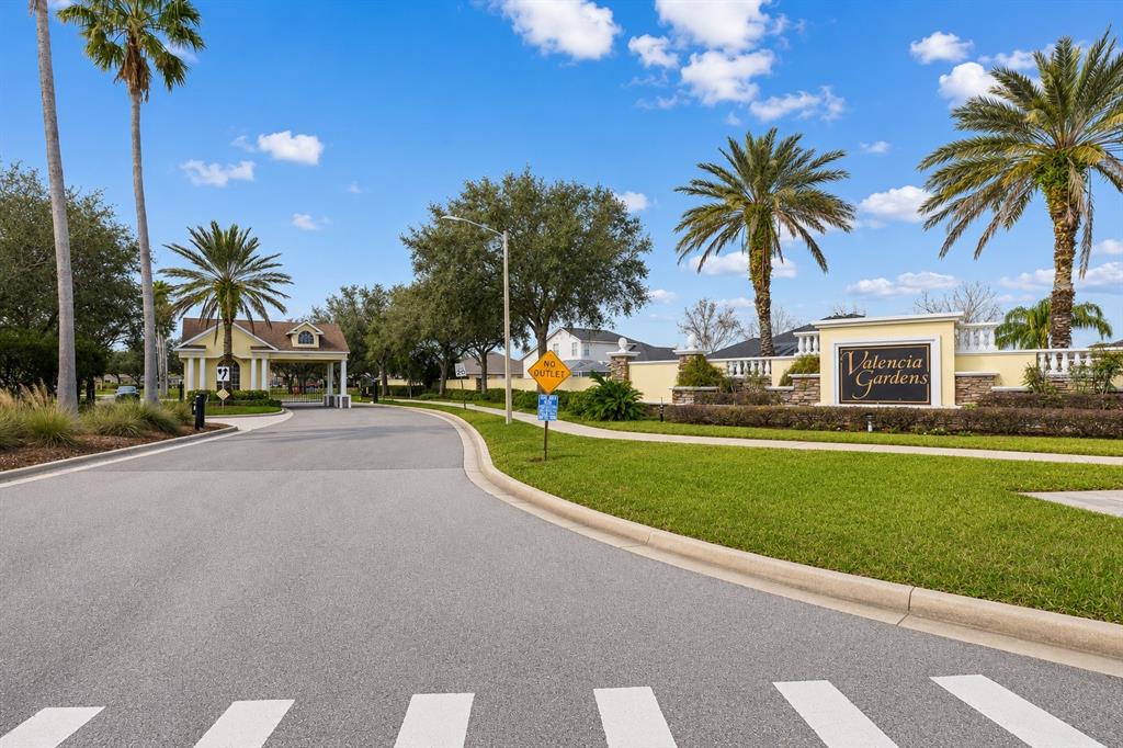 A paved road leads to the gated entrance and signage of the Valencia Gardens community — 22623 CLIFFSIDE WAY, LAND O LAKES, FL