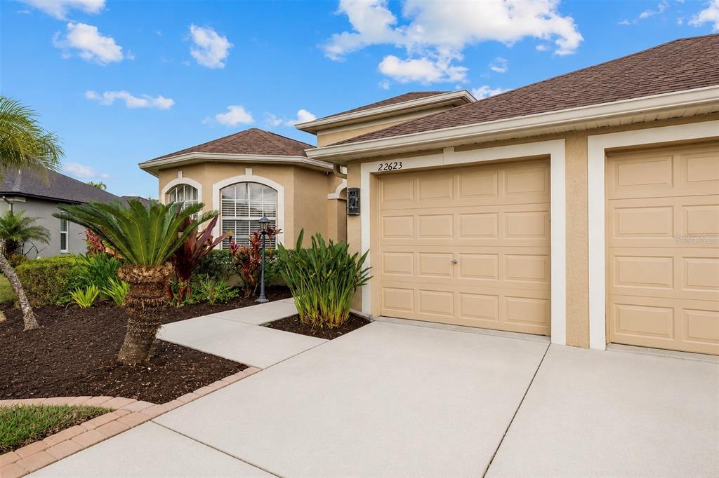 A beige house exterior features a two-car garage, a concrete driveway, and landscaped front gardens — 22623 CLIFFSIDE WAY, LAND O LAKES, FL
