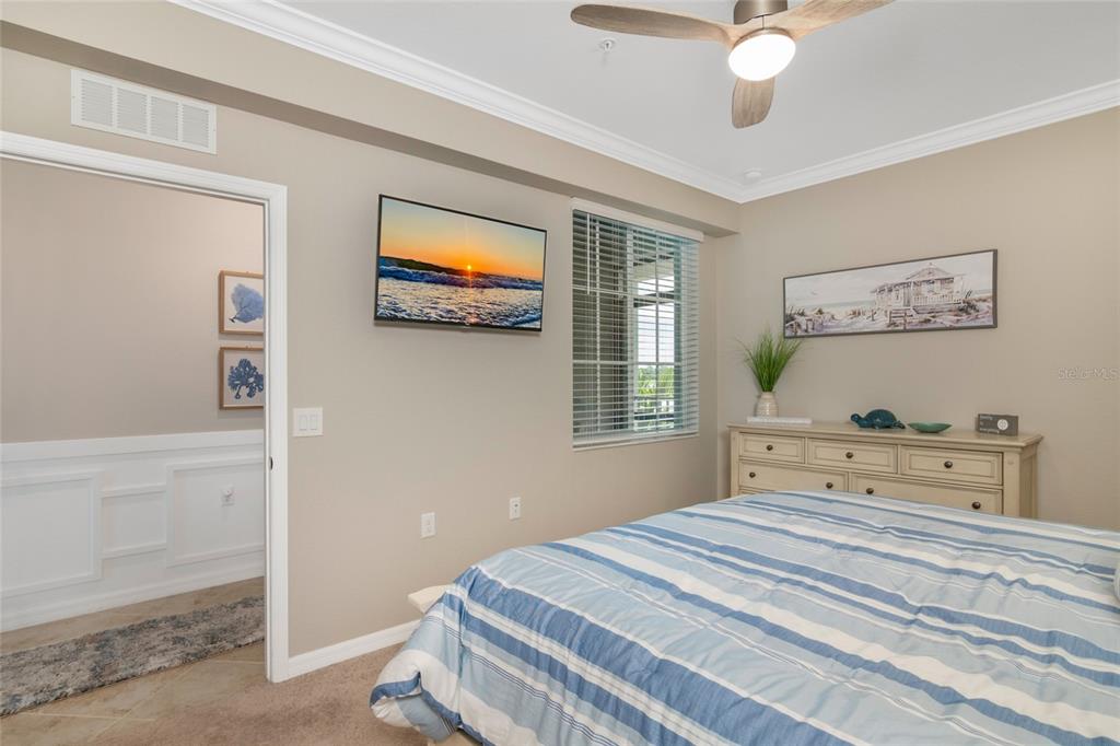 A bedroom features a striped bedspread, a wall-mounted television, a dresser, and a ceiling fan — 14051 HERITAGE LANDING BOULEVARD UNIT 523, PUNTA GORDA, FL