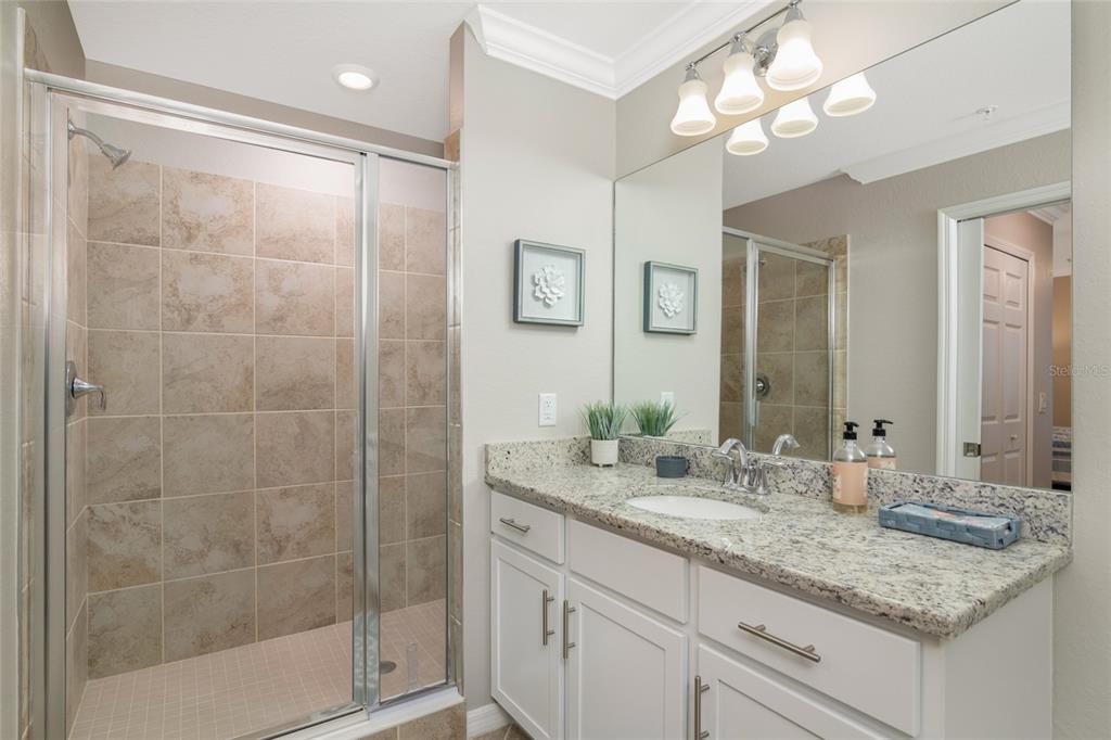 A bathroom features a tiled walk-in shower, a granite vanity countertop, and a large mirror — 14051 HERITAGE LANDING BOULEVARD UNIT 523, PUNTA GORDA, FL