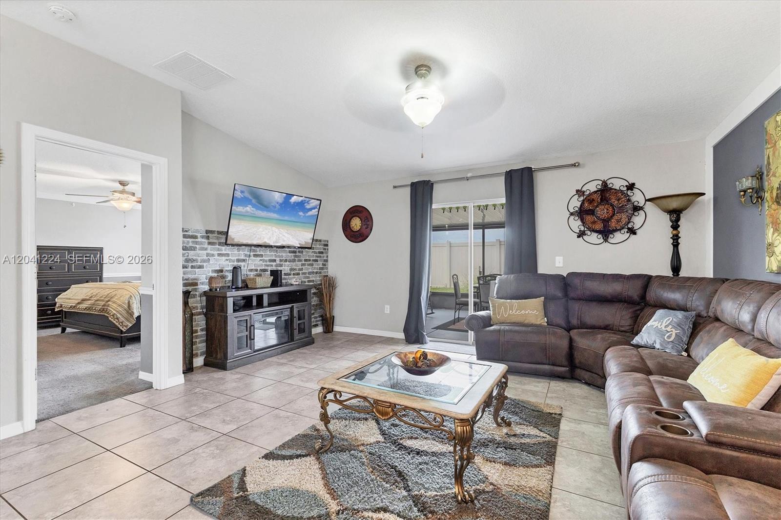 A living room features tile flooring, a brick accent wall, and a brown sectional sofa — 16505 Myrtle, Tampa FL 33598, TAMPA, FL