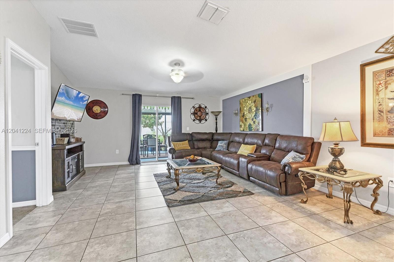 A living room features a large brown sectional sofa, tile flooring, and a sliding glass door — 16505 Myrtle, Tampa FL 33598, TAMPA, FL