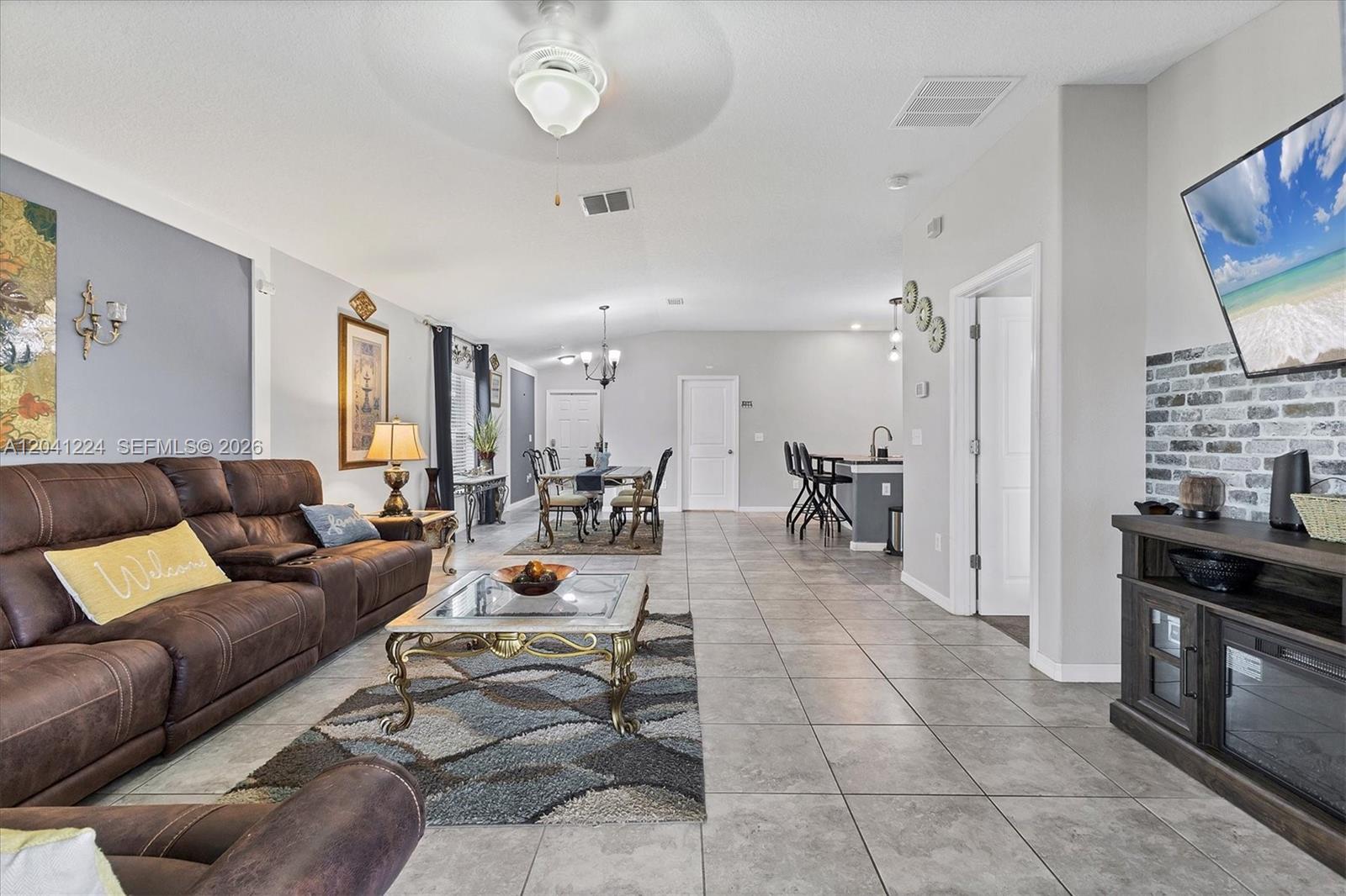 An open-concept living and dining area features tile flooring, a brown sofa, and a television — 16505 Myrtle, Tampa FL 33598, TAMPA, FL