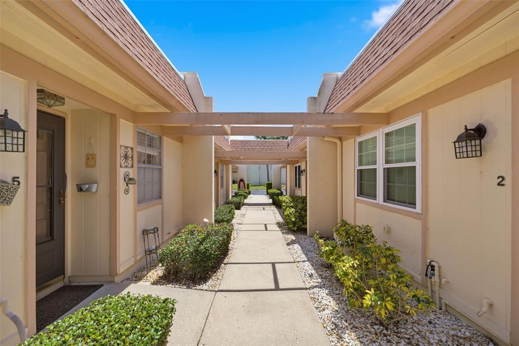 A concrete walkway leads between two tan residential units with brown roofs and pergolas — 11210 CARRIAGE HILL DRIVE UNIT 5, PORT RICHEY, FL