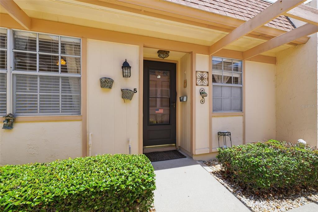 The exterior of a home features a dark front door, windows, and a small walkway — 11210 CARRIAGE HILL DRIVE UNIT 5, PORT RICHEY, FL