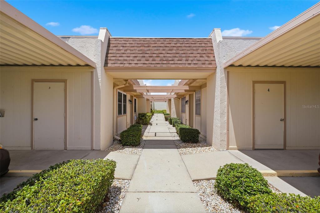 A concrete walkway leads between two rows of single-story residential units with covered entryways — 11210 CARRIAGE HILL DRIVE UNIT 5, PORT RICHEY, FL