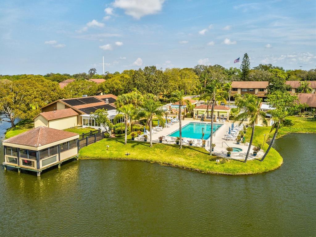 An aerial view shows a community pool and clubhouse situated on a lakefront lot — 3843 LIGHTHOUSE WAY, NEW PORT RICHEY, FL