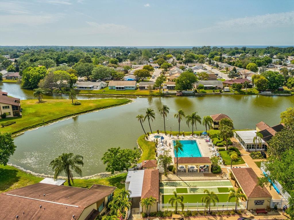 An aerial view of a community pool, shuffleboard court, and lake surrounded by residential homes — 3843 LIGHTHOUSE WAY, NEW PORT RICHEY, FL