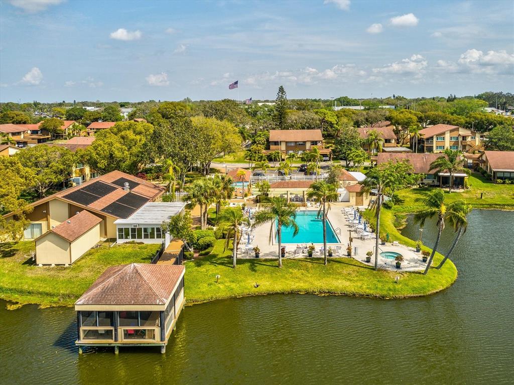 An aerial view shows a community pool and clubhouse situated on a lakefront property — 3843 LIGHTHOUSE WAY, NEW PORT RICHEY, FL