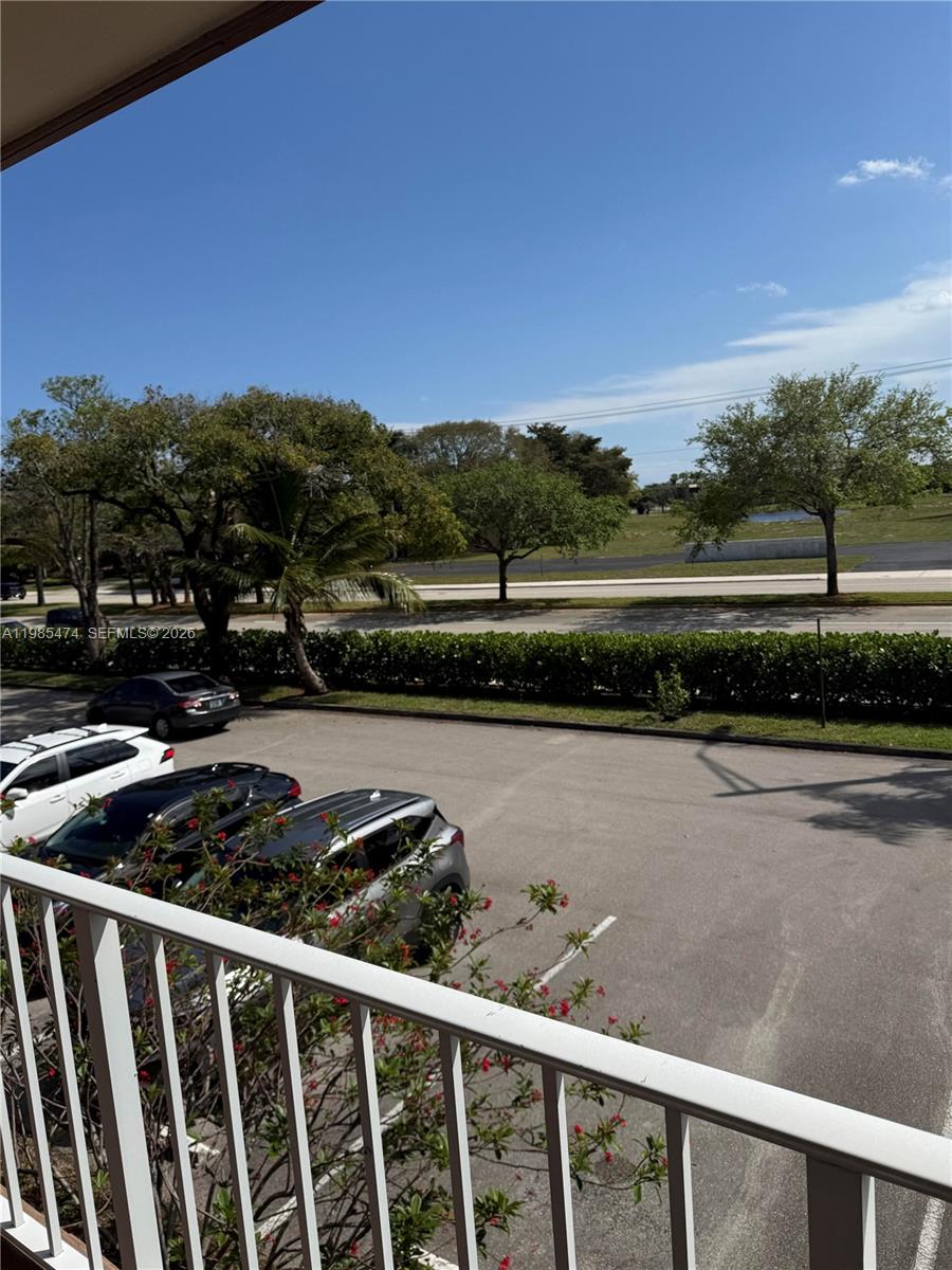 A view from a balcony overlooks a parking lot, trees, and a road — 7605 W Atlantic Blvd # 207, Margate FL 33063, MARGATE, FL