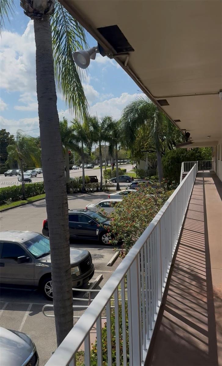 An elevated outdoor walkway overlooks a parking lot with several cars and palm trees — 7605 W Atlantic Blvd # 207, Margate FL 33063, MARGATE, FL