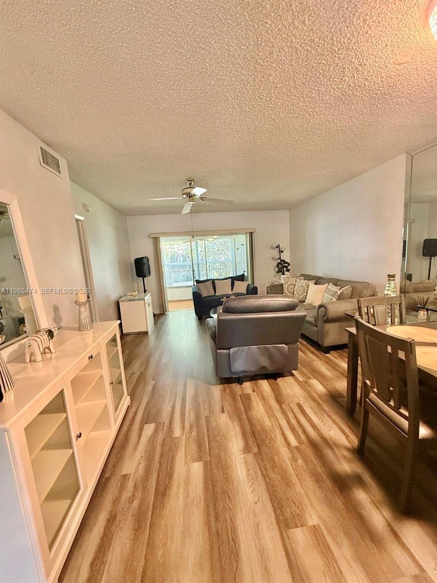 A living room with wood-look flooring, a ceiling fan, and a sliding glass door — 7605 W Atlantic Blvd # 207, Margate FL 33063, MARGATE, FL