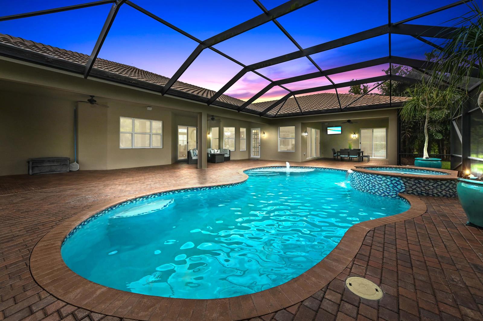 A swimming pool and spa with a brick deck inside a screened-in lanai at dusk — 7777 Eden Ridge Way, West Palm Beach FL 33412, WEST PALM BEACH, FL