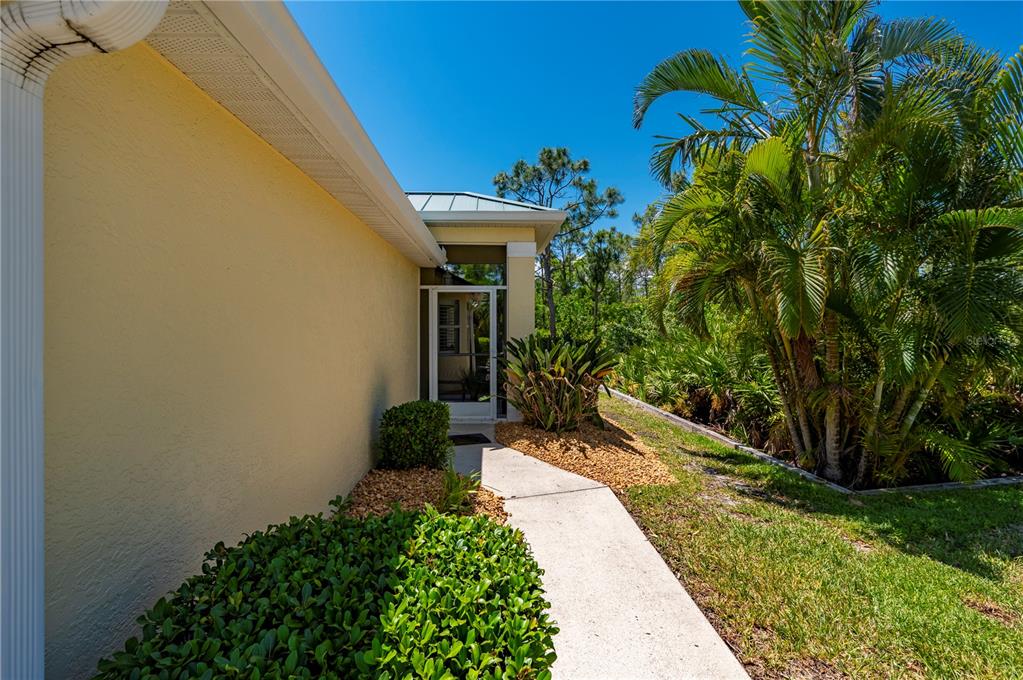 A concrete walkway leads past a yellow house exterior with a palm tree and landscaping — 310 ISLAMORADA BOULEVARD, PUNTA GORDA, FL
