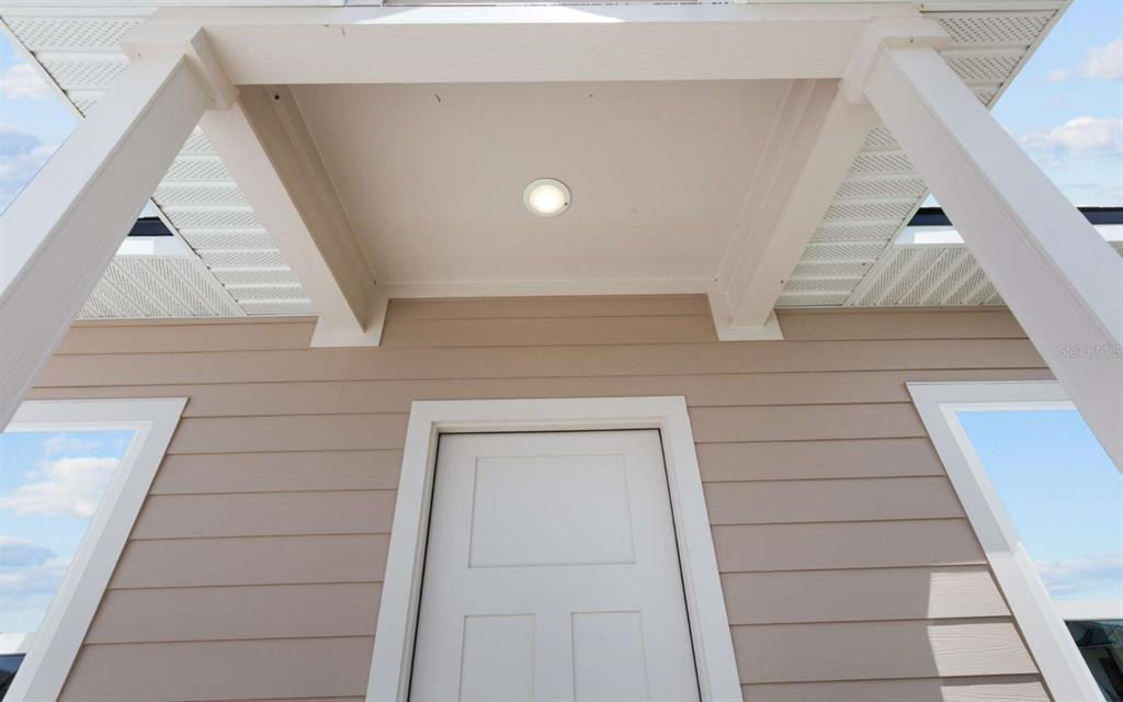 A low-angle view shows a tan-sided house exterior with a white door and porch ceiling — 206 MESA STREET NW, LIVE OAK, FL