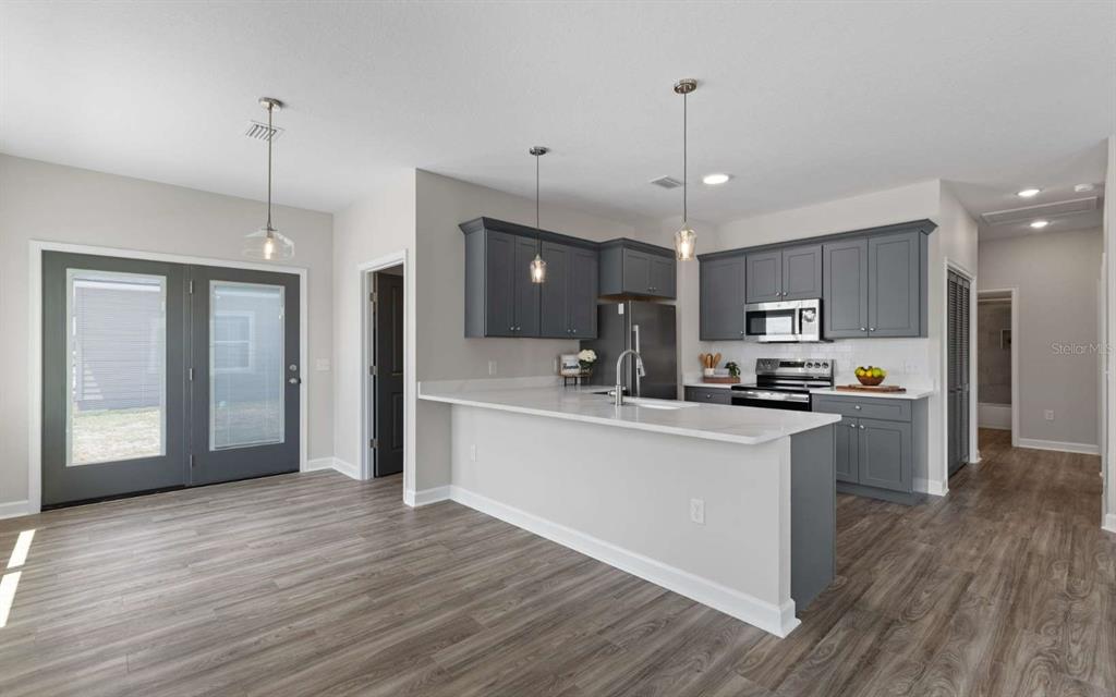 A kitchen with grey cabinets, white countertops, and wood-look flooring opens to a dining area — 206 MESA STREET NW, LIVE OAK, FL