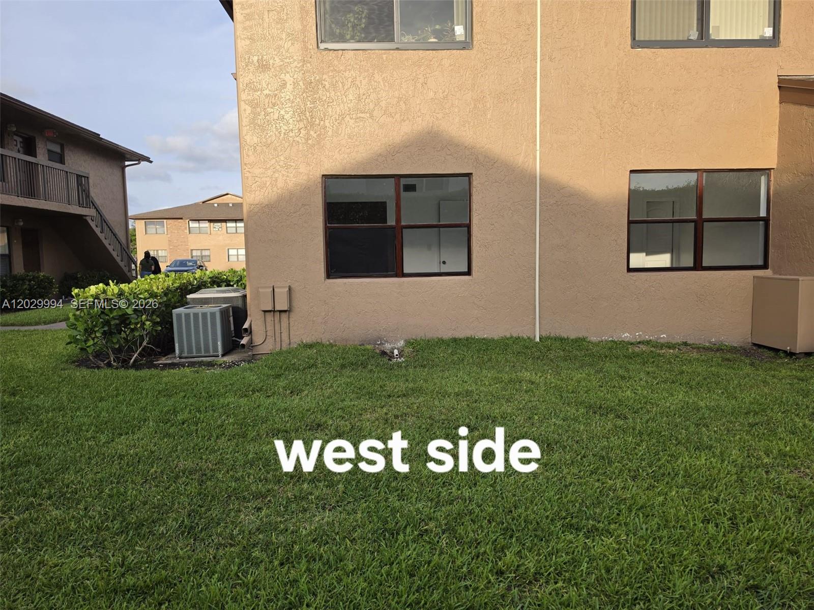 The exterior of a tan multi-story apartment building features two windows and an air conditioner — SUNRISE, FL