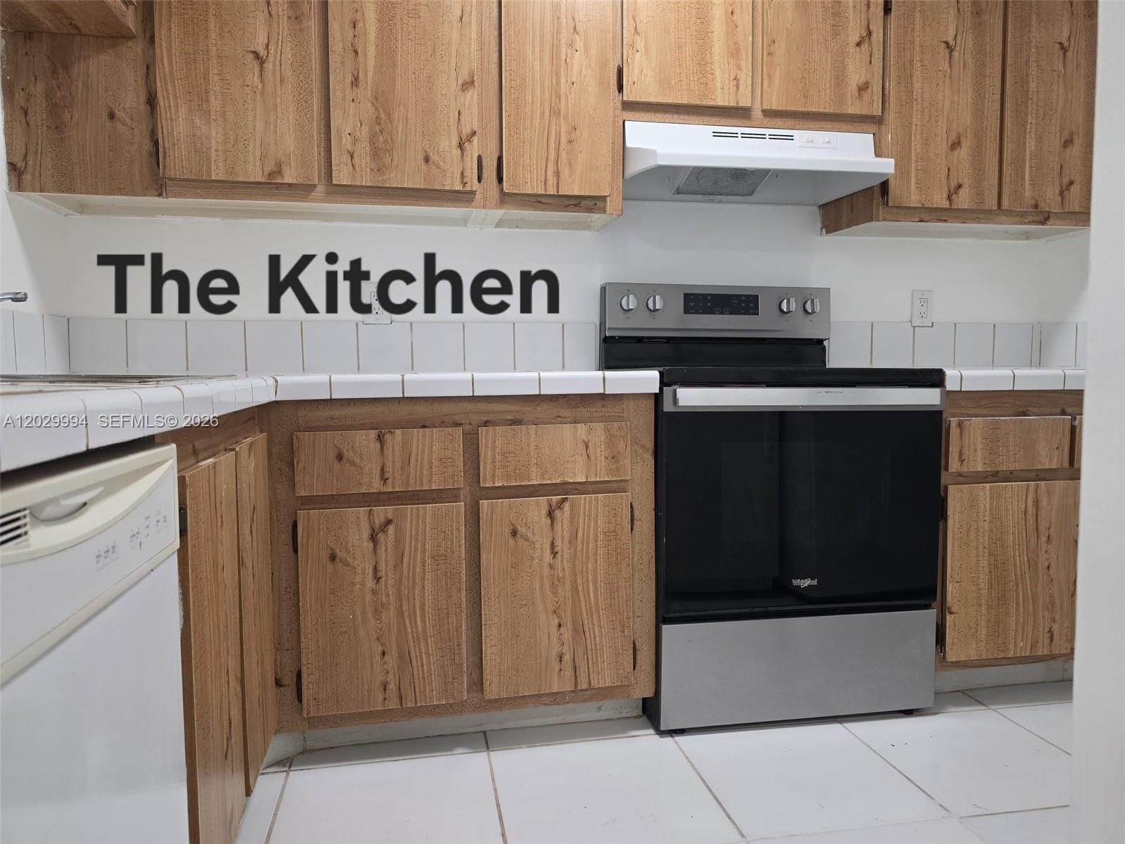 A kitchen features wood-grain cabinets, white tile countertops, and stainless steel appliances — SUNRISE, FL
