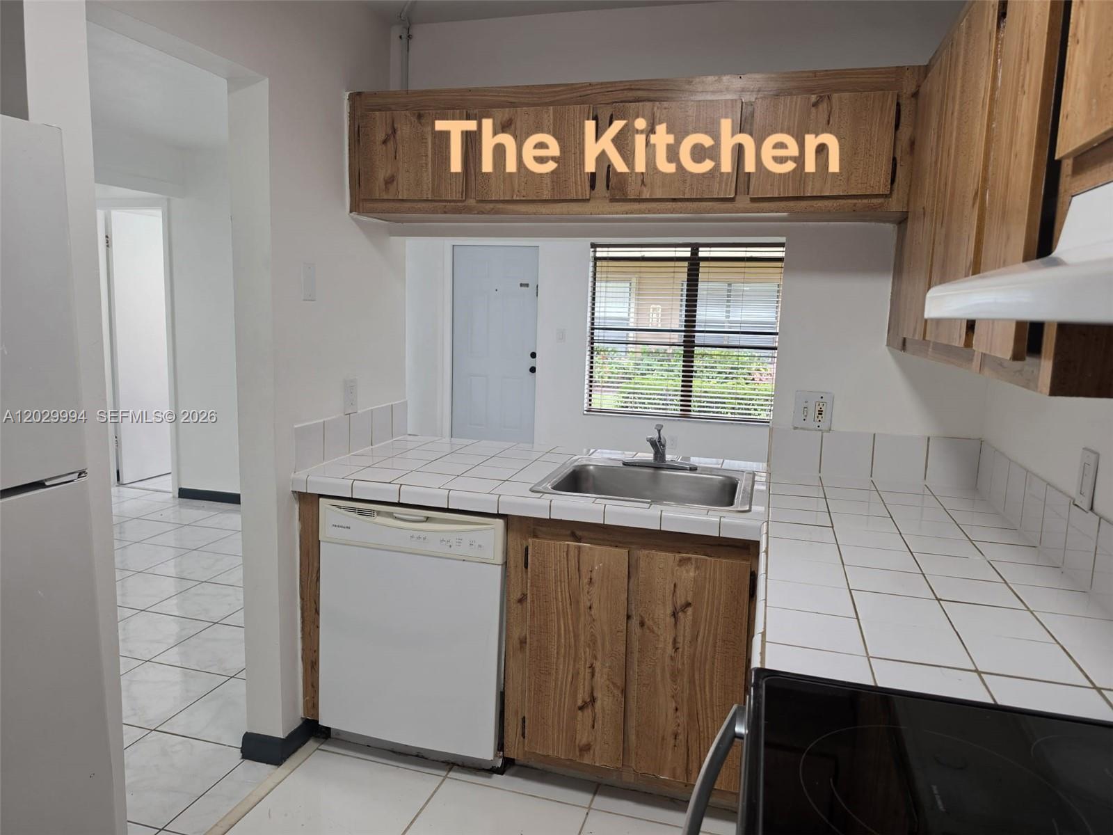 A kitchen features wood cabinets, white tiled countertops, a stainless steel sink, and a dishwasher — SUNRISE, FL