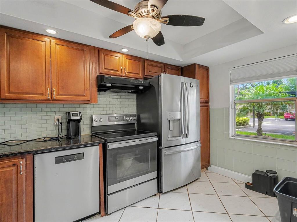 A kitchen features wood cabinets, stainless steel appliances, a subway tile backsplash, and tile flooring — 2653 WOODGATE LANE UNIT E-3, SARASOTA, FL
