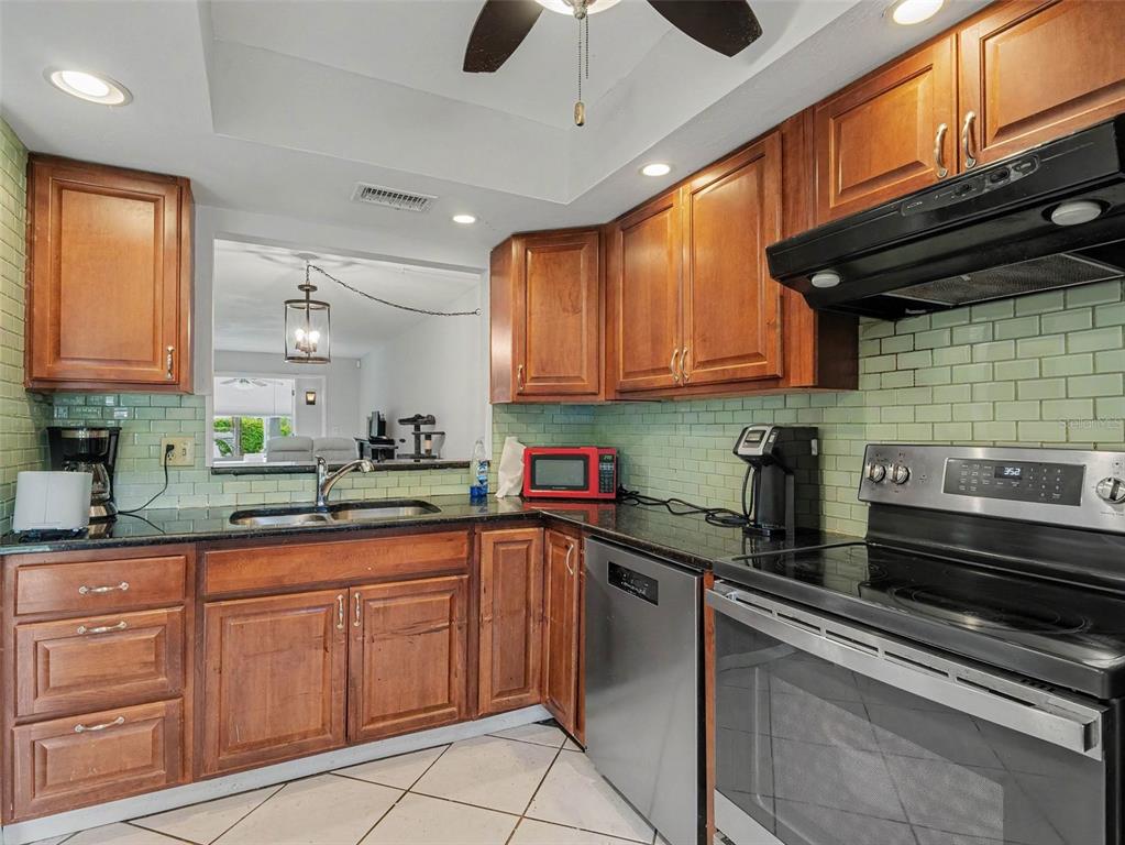 A kitchen with wood cabinets, green subway tile backsplash, black countertops, and stainless steel appliances — 2653 WOODGATE LANE UNIT E-3, SARASOTA, FL