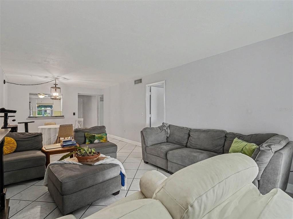 A living room features gray sectional sofas, white tile flooring, and an adjacent dining area — 2653 WOODGATE LANE UNIT E-3, SARASOTA, FL