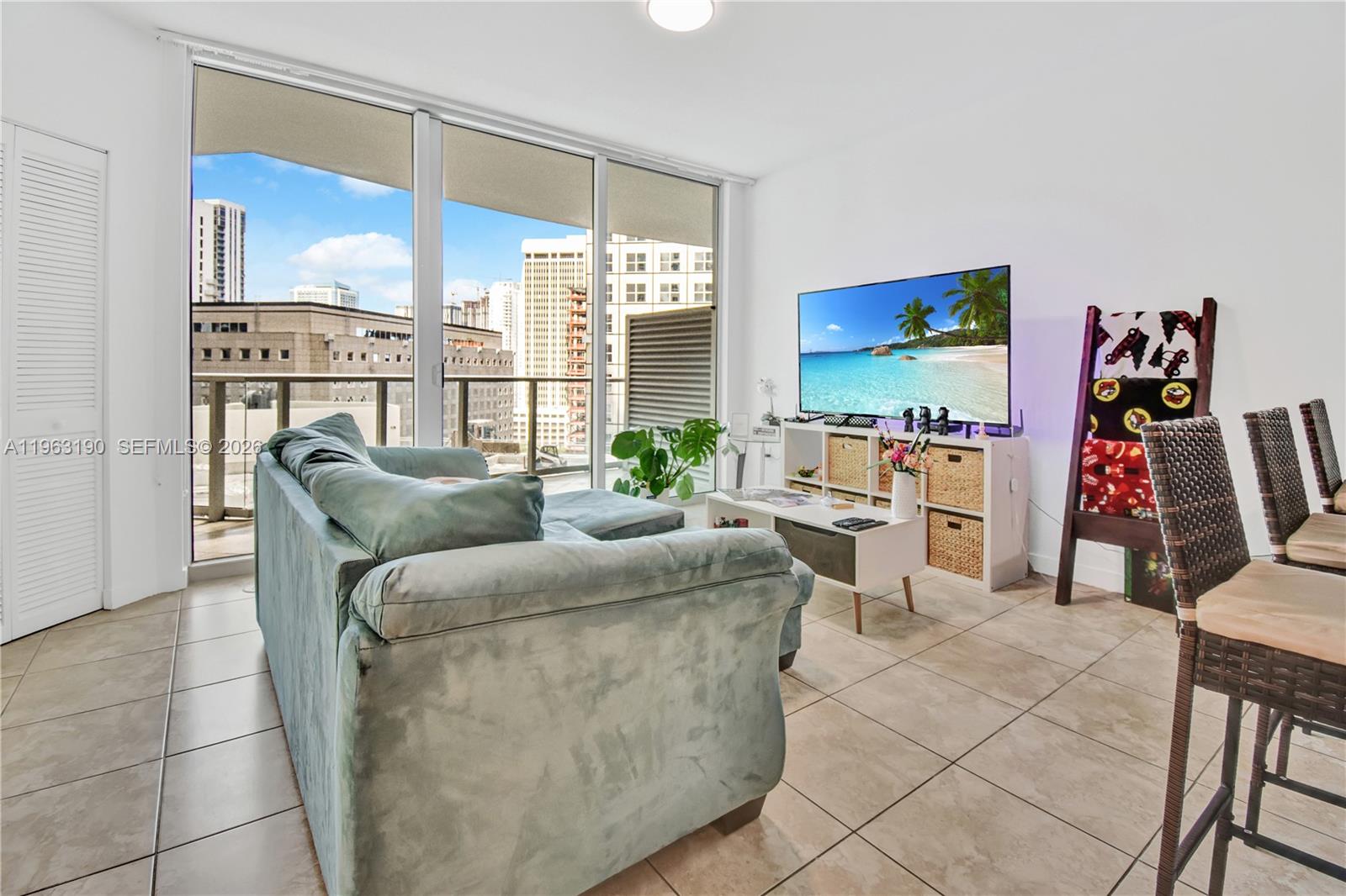 A living room features a light blue sectional sofa, a television stand, and floor-to-ceiling windows — 300 S Biscayne Blvd # 1405, Miami FL 33131, MIAMI, FL