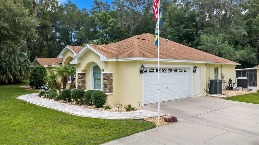 A yellow house with a two-car garage, stone accents, and a paved walkway — 17261 SE 101ST AVENUE ROAD, SUMMERFIELD, FL