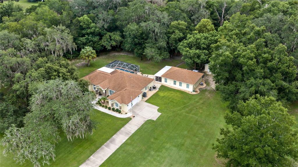 An aerial view shows a house with a pool enclosure and a detached garage among trees — 17261 SE 101ST AVENUE ROAD, SUMMERFIELD, FL