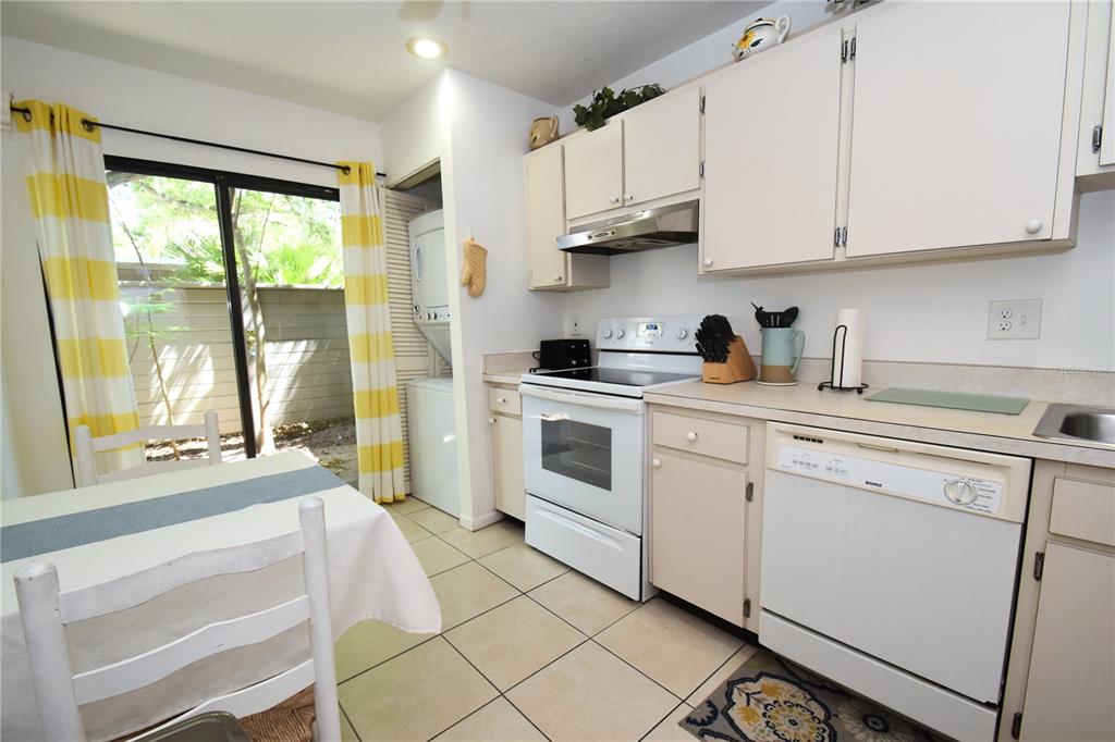 A kitchen with white appliances, beige cabinets, tile flooring, and a sliding glass door — 1620 BOATHOUSE CIRCLE UNIT GR103, SARASOTA, FL