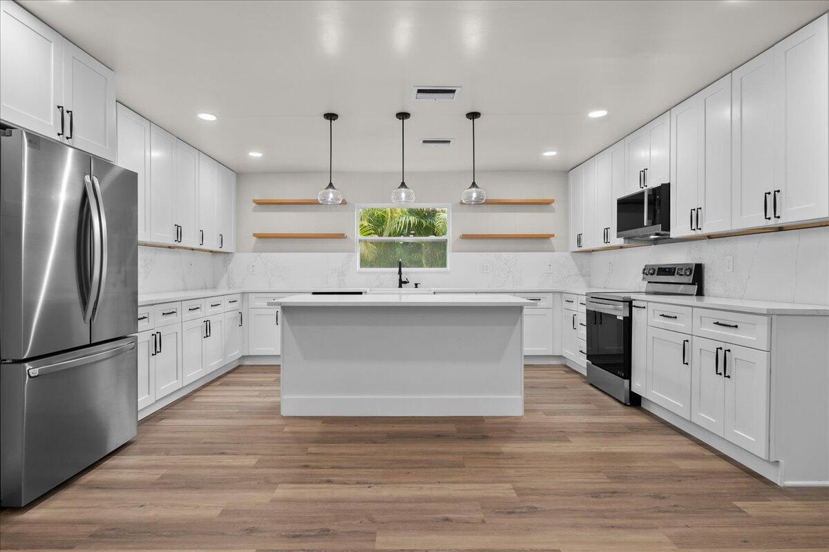 A modern white kitchen features stainless steel appliances, an island, and wood-look flooring — 426 Bayberry Drive, West Palm Beach FL 33403, WEST PALM BEACH, FL