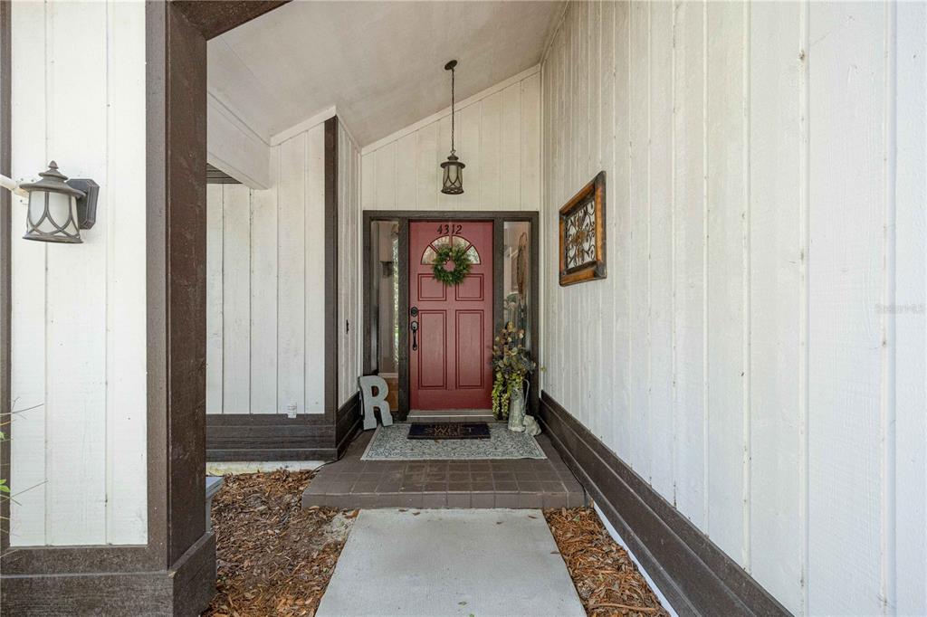 A red front door with a wreath is centered under a covered entryway — 4312 NW 12TH PLACE, GAINESVILLE, FL