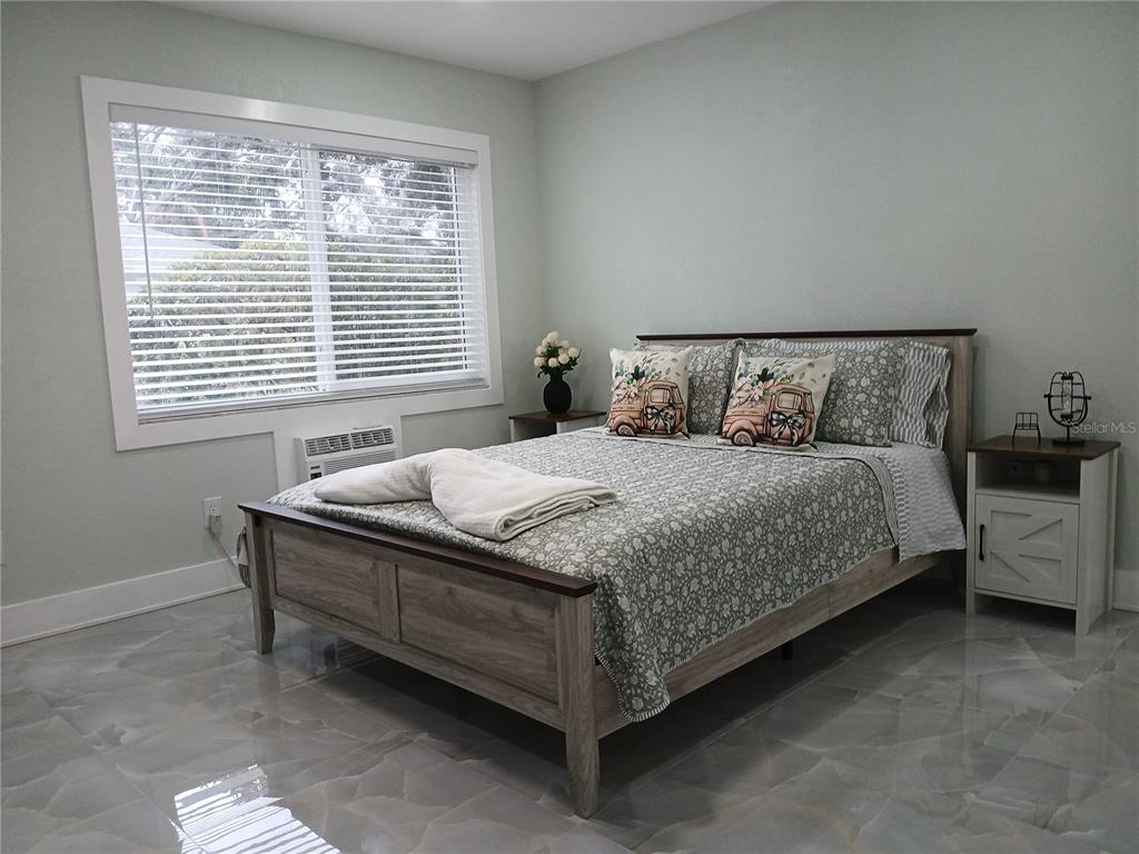 A bedroom features a wooden bed frame, light green walls, and glossy tiled flooring — 4129 DOLPHIN DRIVE UNIT 1, TAMPA, FL