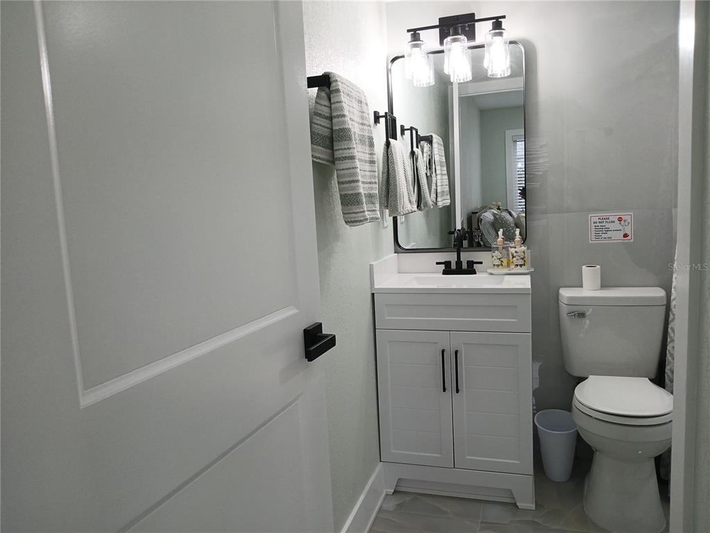 A small bathroom features a white vanity, a rectangular mirror, and a toilet — 4129 DOLPHIN DRIVE UNIT 1, TAMPA, FL