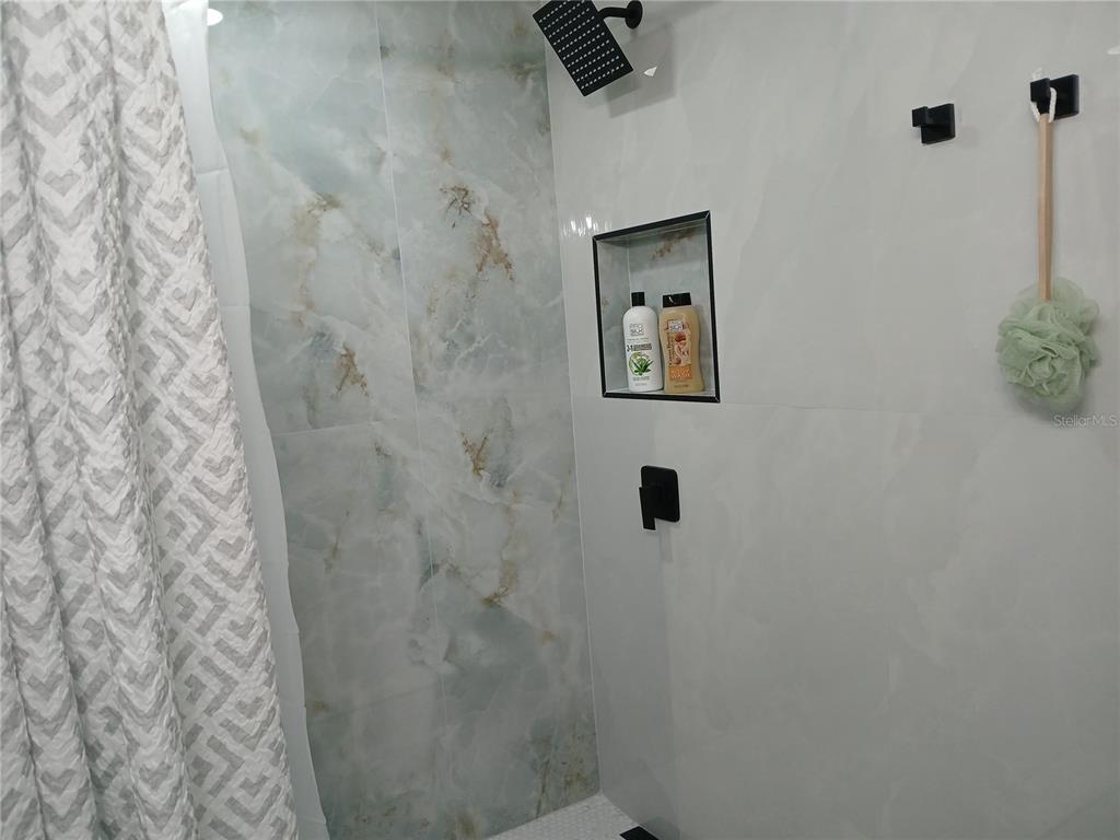A shower features white and marble-patterned tile walls, a black showerhead, and a recessed niche — 4129 DOLPHIN DRIVE UNIT 1, TAMPA, FL