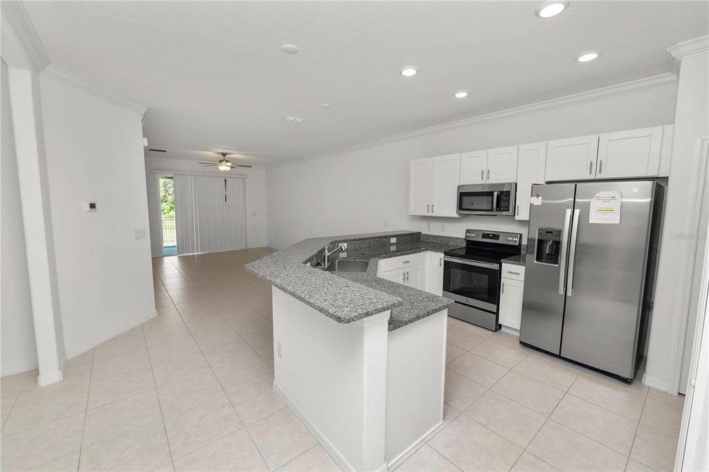 A kitchen with granite countertops and stainless steel appliances opens into a tiled living area — 6851 RIPPLE POND LOOP, ZEPHYRHILLS, FL