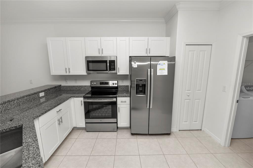A kitchen with white cabinets, granite countertops, stainless steel appliances, and tile flooring — 6851 RIPPLE POND LOOP, ZEPHYRHILLS, FL