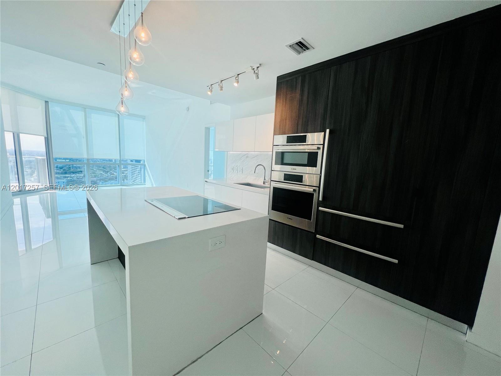 A modern kitchen features a white island, dark wood cabinetry, and stainless steel built-in appliances — 851 NE 1st Av # 2808, Miami FL 33132, MIAMI, FL