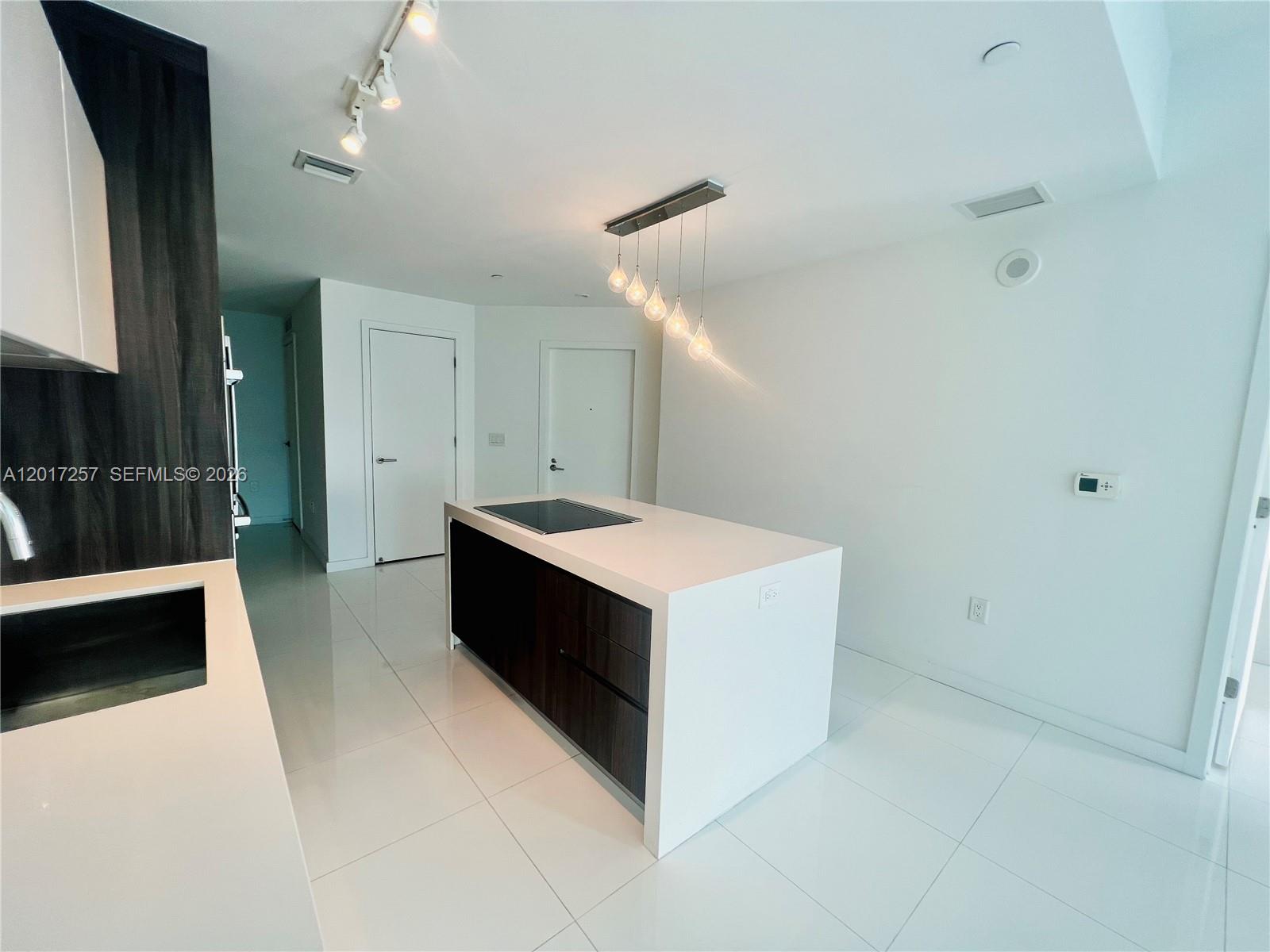 A modern kitchen features a central island with a cooktop, dark cabinetry, and white flooring — 851 NE 1st Av # 2808, Miami FL 33132, MIAMI, FL