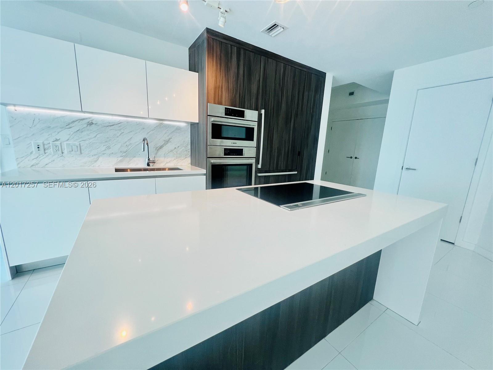 A modern kitchen features a white island, dark wood cabinetry, and marble-patterned backsplash — 851 NE 1st Av # 2808, Miami FL 33132, MIAMI, FL