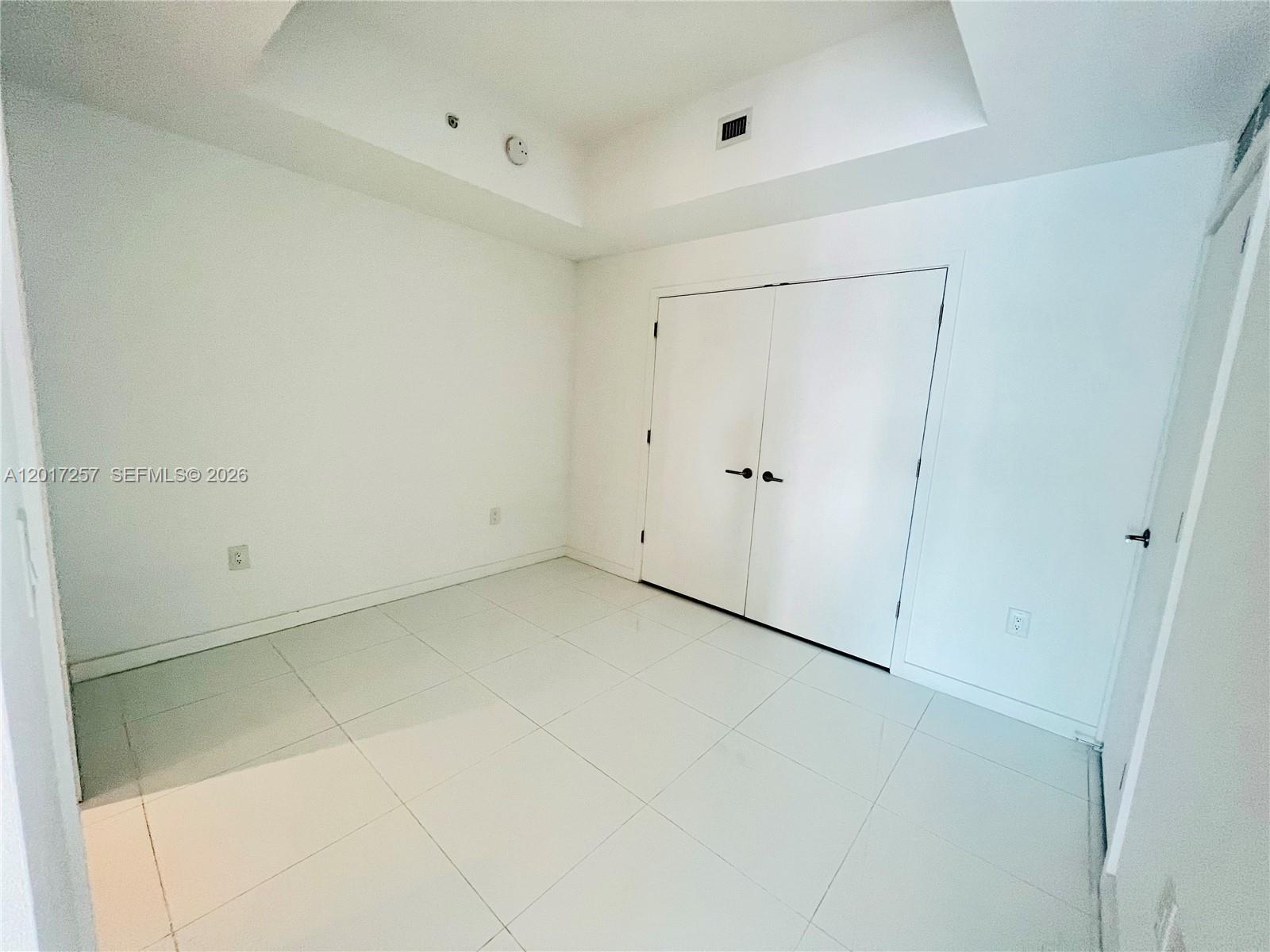 An empty room features white walls, white tile flooring, and a set of double closet doors — 851 NE 1st Av # 2808, Miami FL 33132, MIAMI, FL