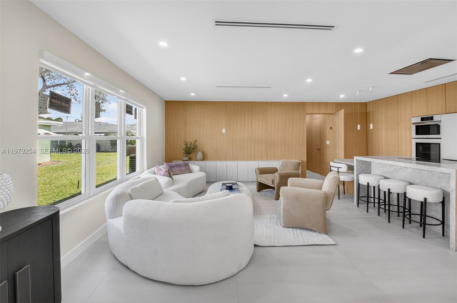 A modern living room features curved white sofas, beige armchairs, and wood-paneled walls — 3240 Park Ln # D, Boynton Beach FL 33435, BOYNTON BEACH, FL