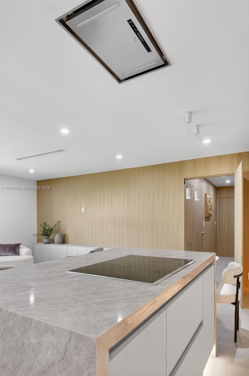 A modern kitchen features a marble-topped island with a cooktop and a wood-paneled wall — 3240 Park Ln # D, Boynton Beach FL 33435, BOYNTON BEACH, FL
