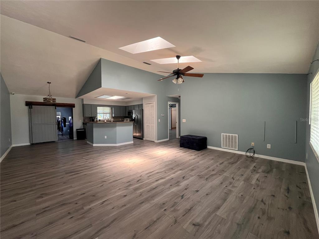 A spacious living room with vaulted ceilings, skylights, and light wood-look flooring — 2511 MILTON AVENUE, NEW SMYRNA BEACH, FL