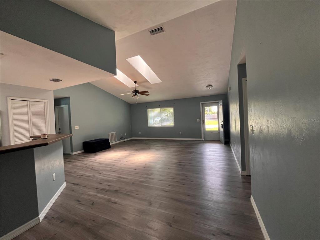 A spacious living room features vaulted ceilings, skylights, light blue walls, and wood-look flooring — 2511 MILTON AVENUE, NEW SMYRNA BEACH, FL
