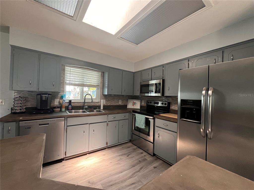 A kitchen features gray cabinets, stainless steel appliances, and wood-look flooring under a skylight — 2511 MILTON AVENUE, NEW SMYRNA BEACH, FL
