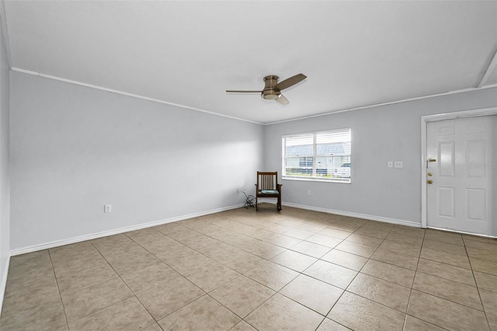An empty room with light gray walls, tan tile flooring, a ceiling fan, and a chair — 11905 BAYONET LANE, NEW PORT RICHEY, FL
