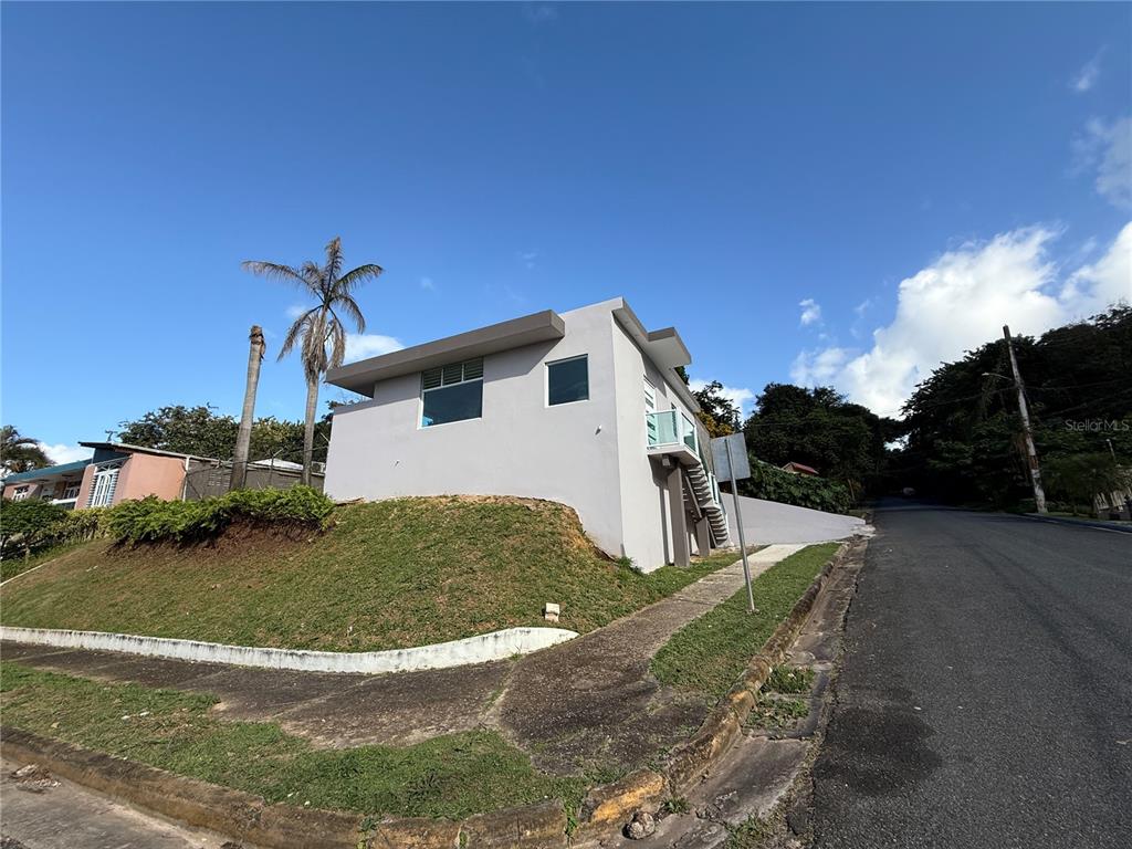 A light gray, modern-style house sits on a sloped corner lot next to a paved road — 21 Andes MONTEREY, SAN JUAN, PR